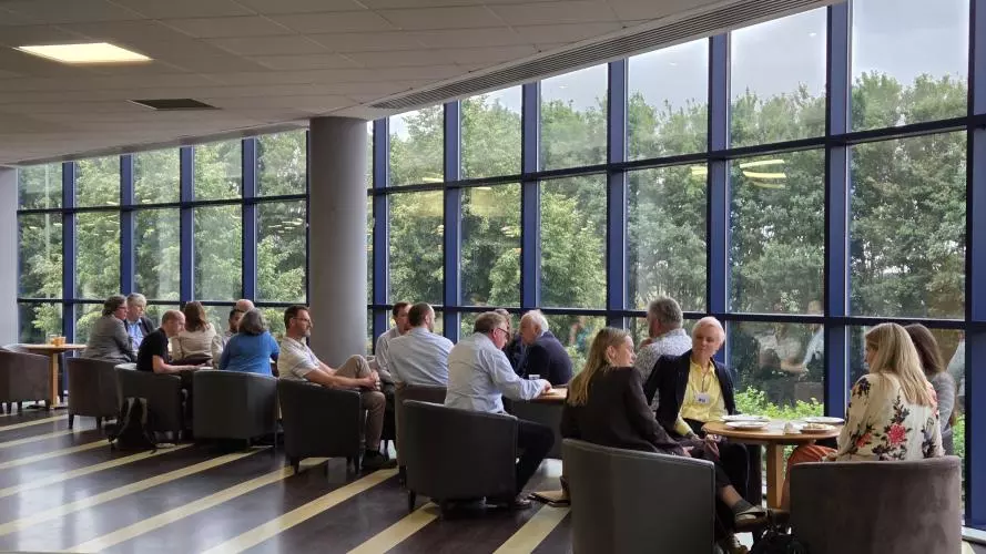 Delegates seated in small groups discussing topics during a networking lunch in a conference venue.