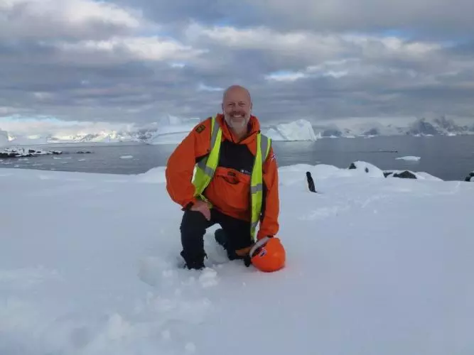 Professor Mike Kendall kneels in the snow during fieldwork in Antarctica.